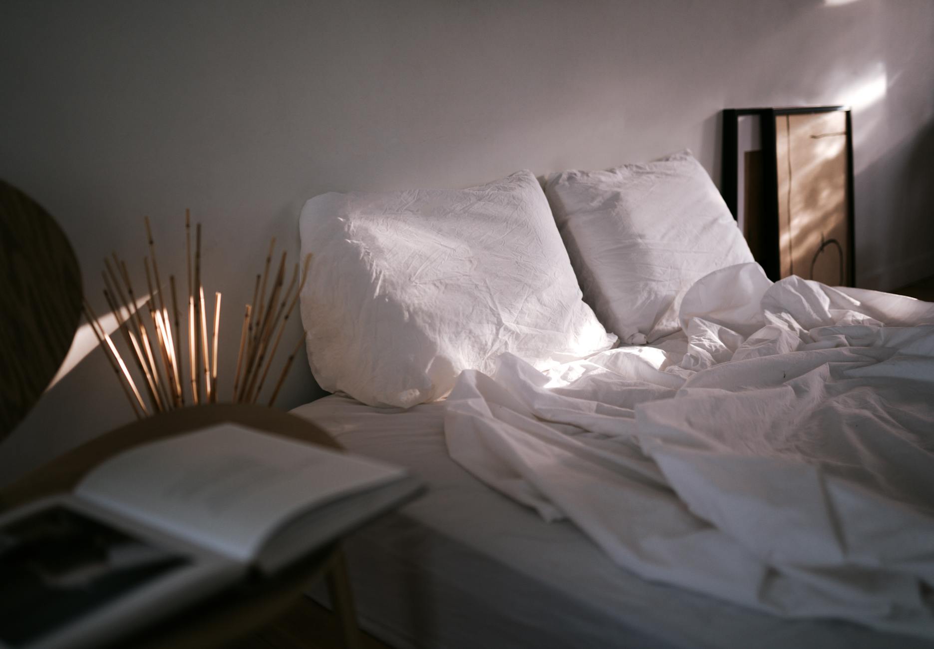 Zerwühlte weiße Bettwäsche im Morgenlicht, daneben ein aufgeschlagenes Buch.